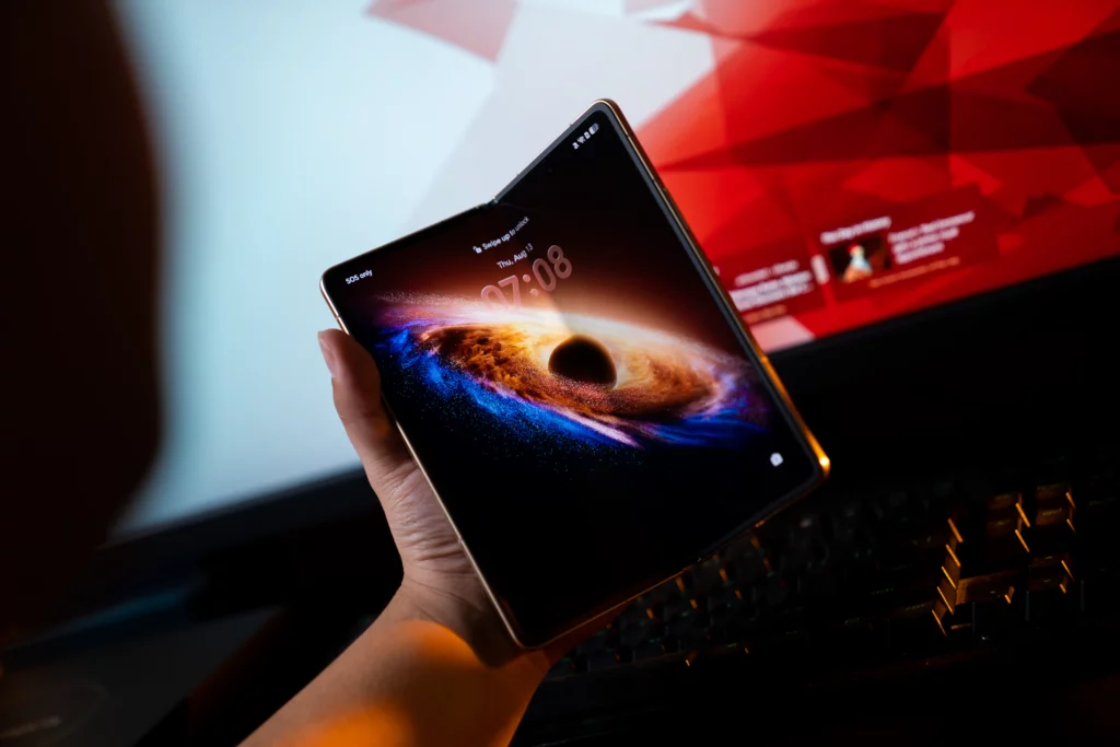 Hand holding the fully unfolded HONOR Magic V6 smartphone displaying a vibrant galaxy and black hole wallpaper on its main inner screen against a dark background.