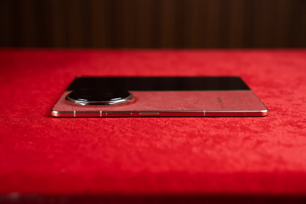 Side view of the unfolded HONOR Magic V6 laying flat on a red surface, showing the right edge with antenna bands, power button, and volume rocker.