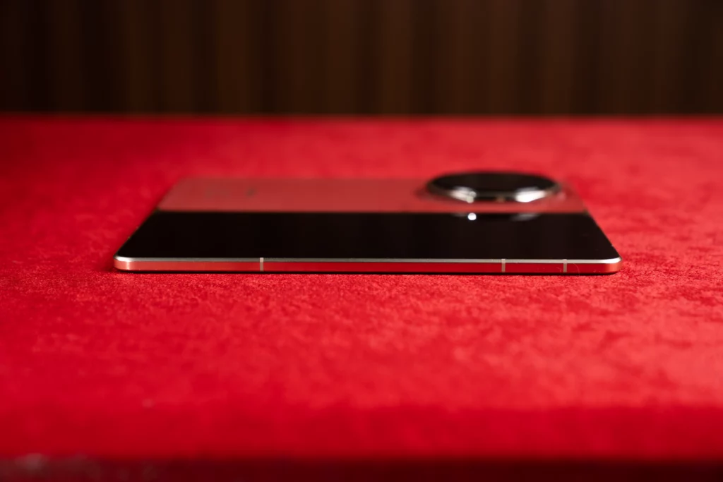 Side view of the unfolded HONOR Magic V6 laying flat on a red surface, highlighting the smooth, thin left edge profile with subtle antenna lines.