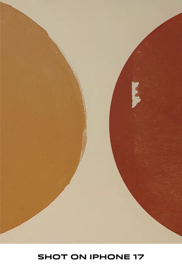 Close-up of an abstract painting featuring yellow and terracotta curved shapes on a beige canvas, labeled "SHOT ON IPHONE 17".
