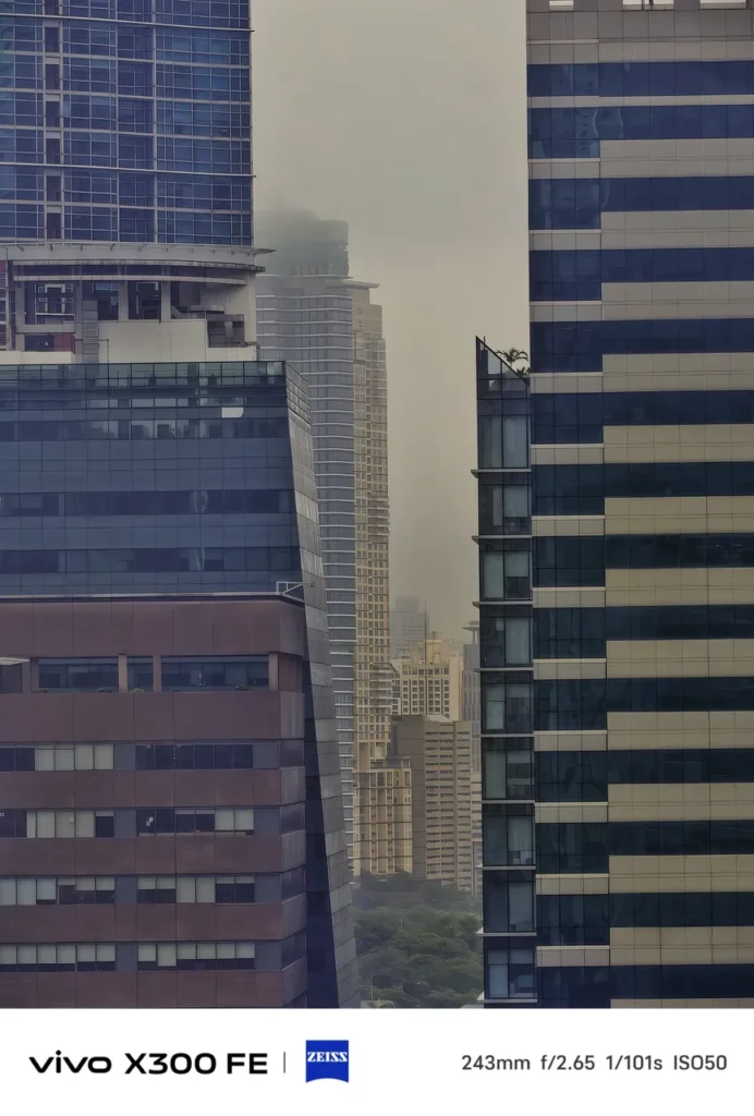 Telephoto shot framing tall city skyscrapers against a hazy, misty sky, captured on the vivo X300 FE with ZEISS camera watermarks.