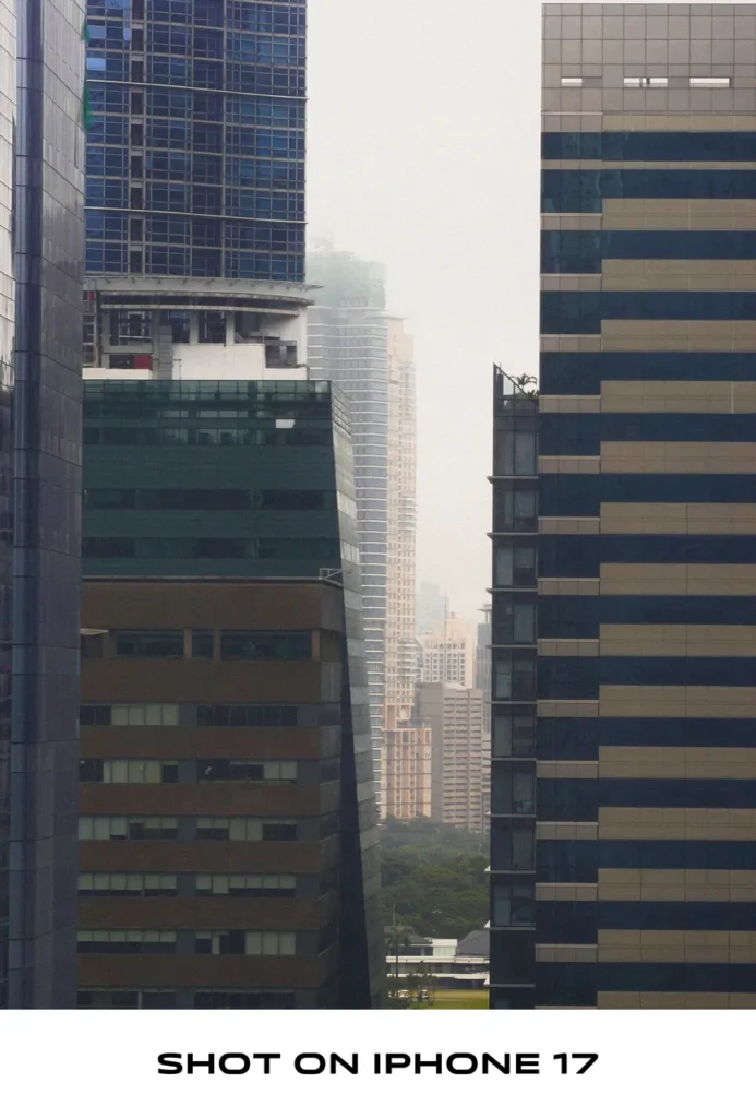 Telephoto shot framing tall city skyscrapers against a hazy, misty sky, labeled "SHOT ON IPHONE 17".
