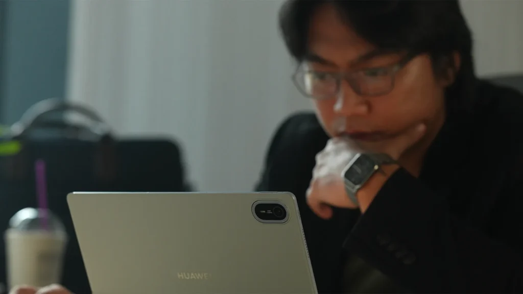 Close-up shot of a man wearing glasses leaning forward thoughtfully while using a light-blue HUAWEI MatePad Air tablet in a workspace setup.