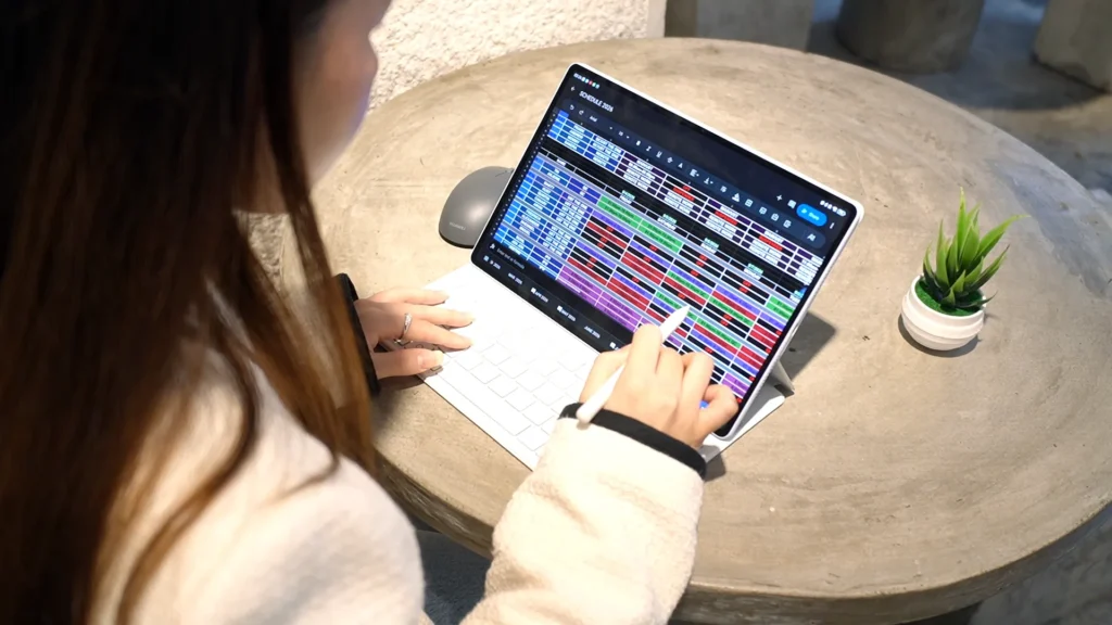Top-down view of a person using the HUAWEI M-Pencil Pro stylus to edit a complex, color-coded schedule spreadsheet on the HUAWEI MatePad Air at a outdoor cafe table.