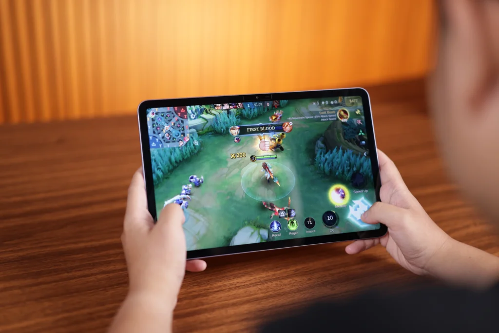 Hands holding the Infinix XPAD 30 Pro horizontally while playing a high-action Mobile Legends multiplayer online battle arena (MOBA) game.