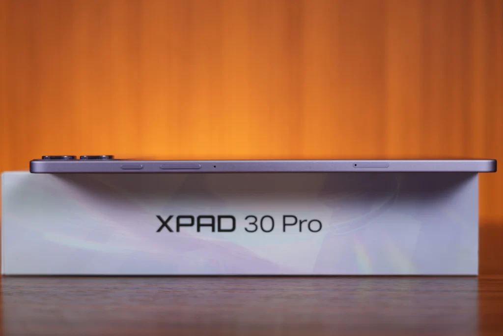 Side profile view of the slim Infinix XPAD 30 Pro resting on its box, showing the volume controls, power button, and SIM card tray slot.