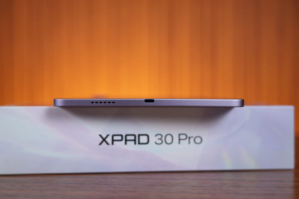 Bottom edge profile of the purple Infinix XPAD 30 Pro sitting on its box, highlighting the USB-C charging port and speaker grilles.