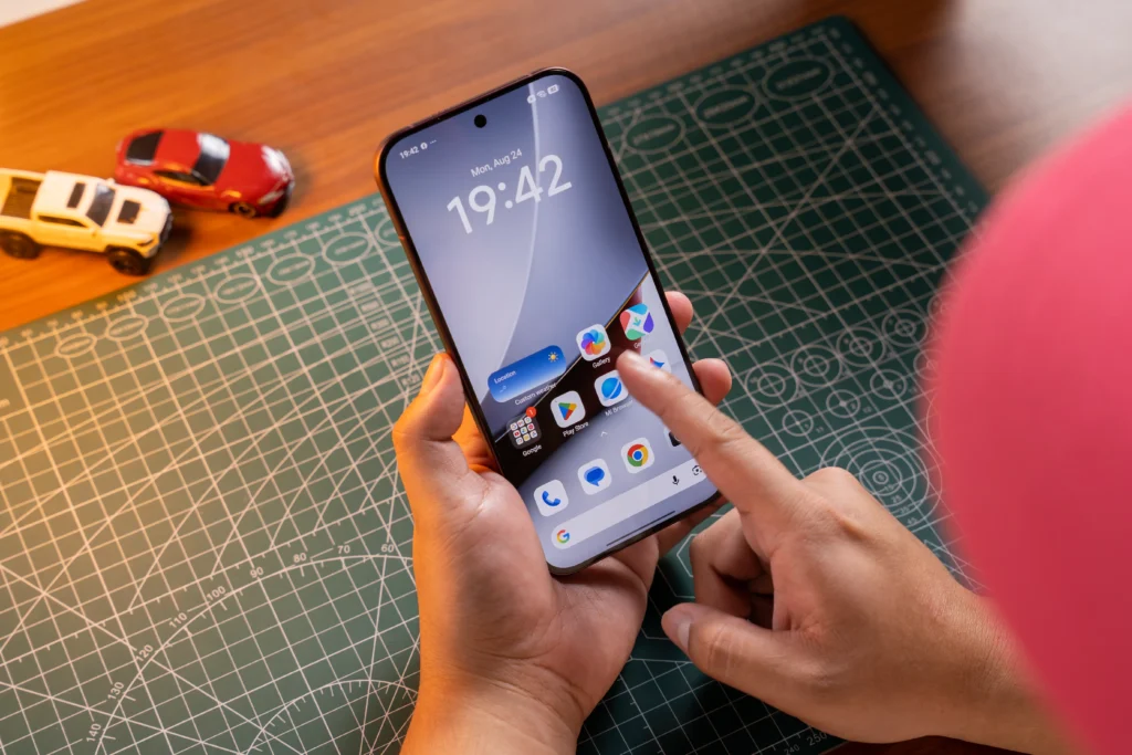 Hands-on shot of a user interacting with the home screen of the POCO F9 Ultra smartphone over a green cutting mat.