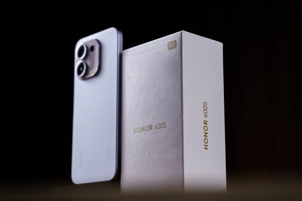 A purple HONOR 600S 5G smartphone sitting upright next to its white retail packaging box with gold lettering on a dark background.