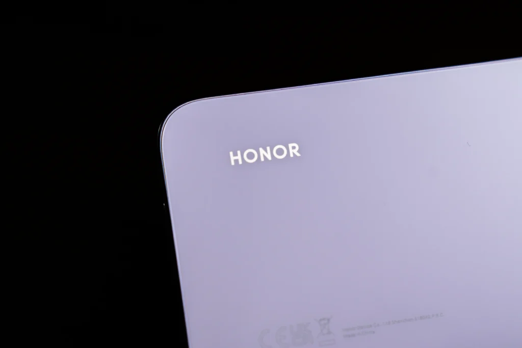 A close-up shot of the top left corner of the purple HONOR 600S 5G back panel showing the silver HONOR branding against a dark background.