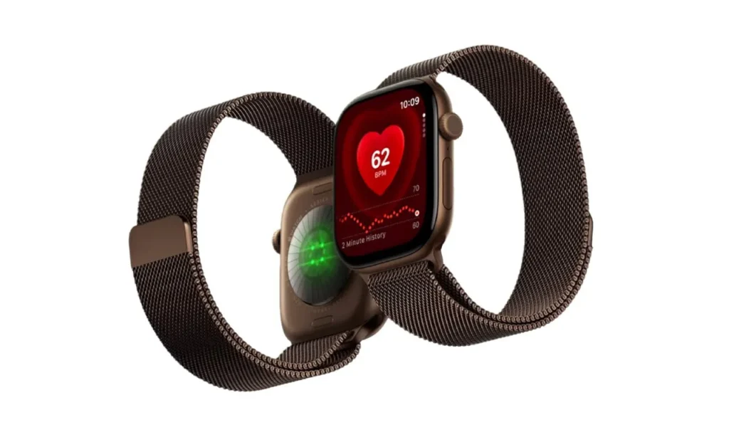 A product shot of two Apple Watches with dark bronze cases and matching Milanese loop mesh bands. The front watch displays a heart rate monitoring screen showing a large red heart, 62 BPM, and a heart rate graph, while the watch behind it shows the back sensor casing with active green LED lights.